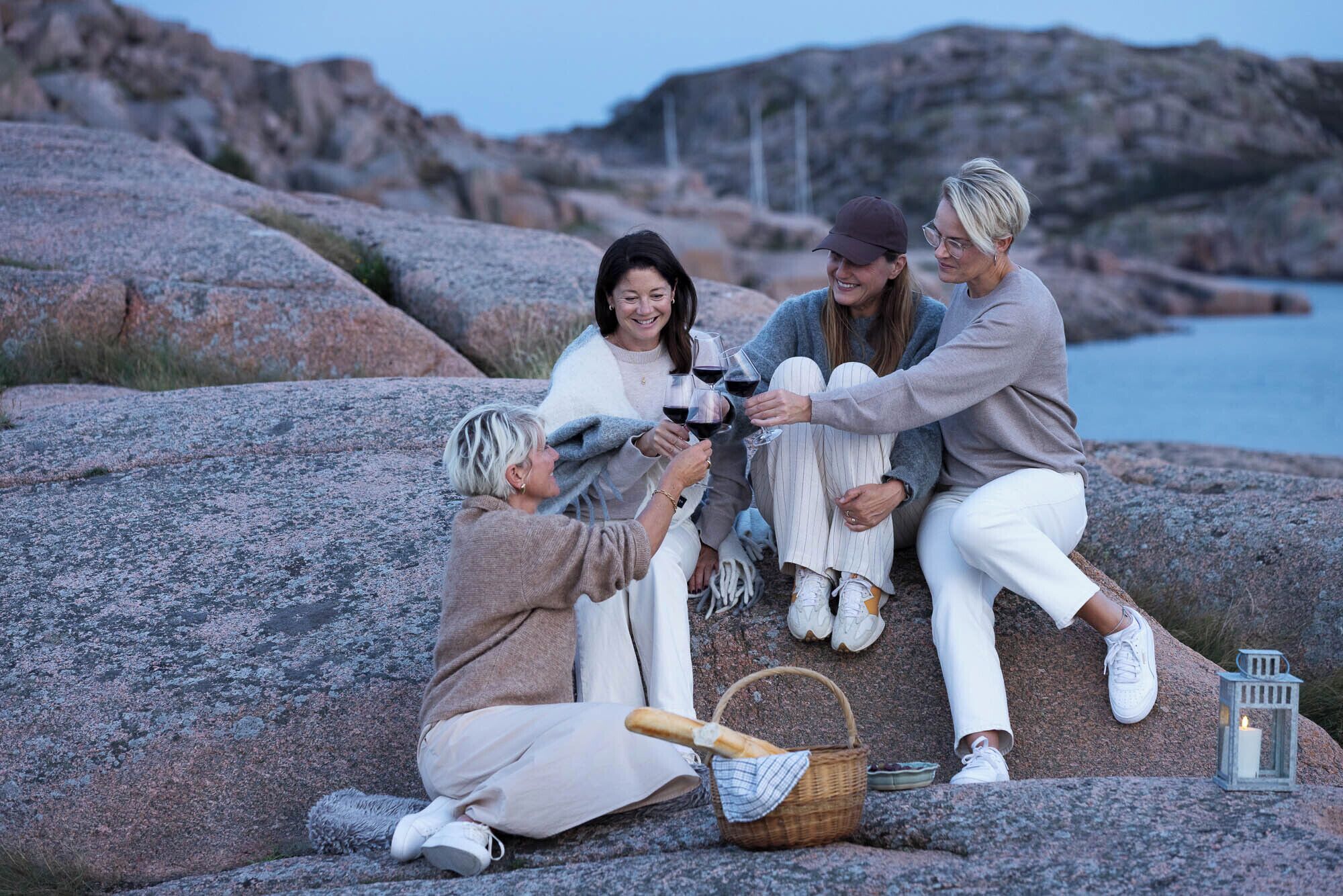 A group of people sitting on rocks by a body of water, with a lantern and a basket nearby.