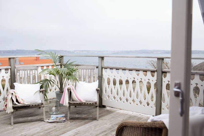 Een balkon met een houten vloer, witte zachte zithoek, een bloempot en een glazen tafel.