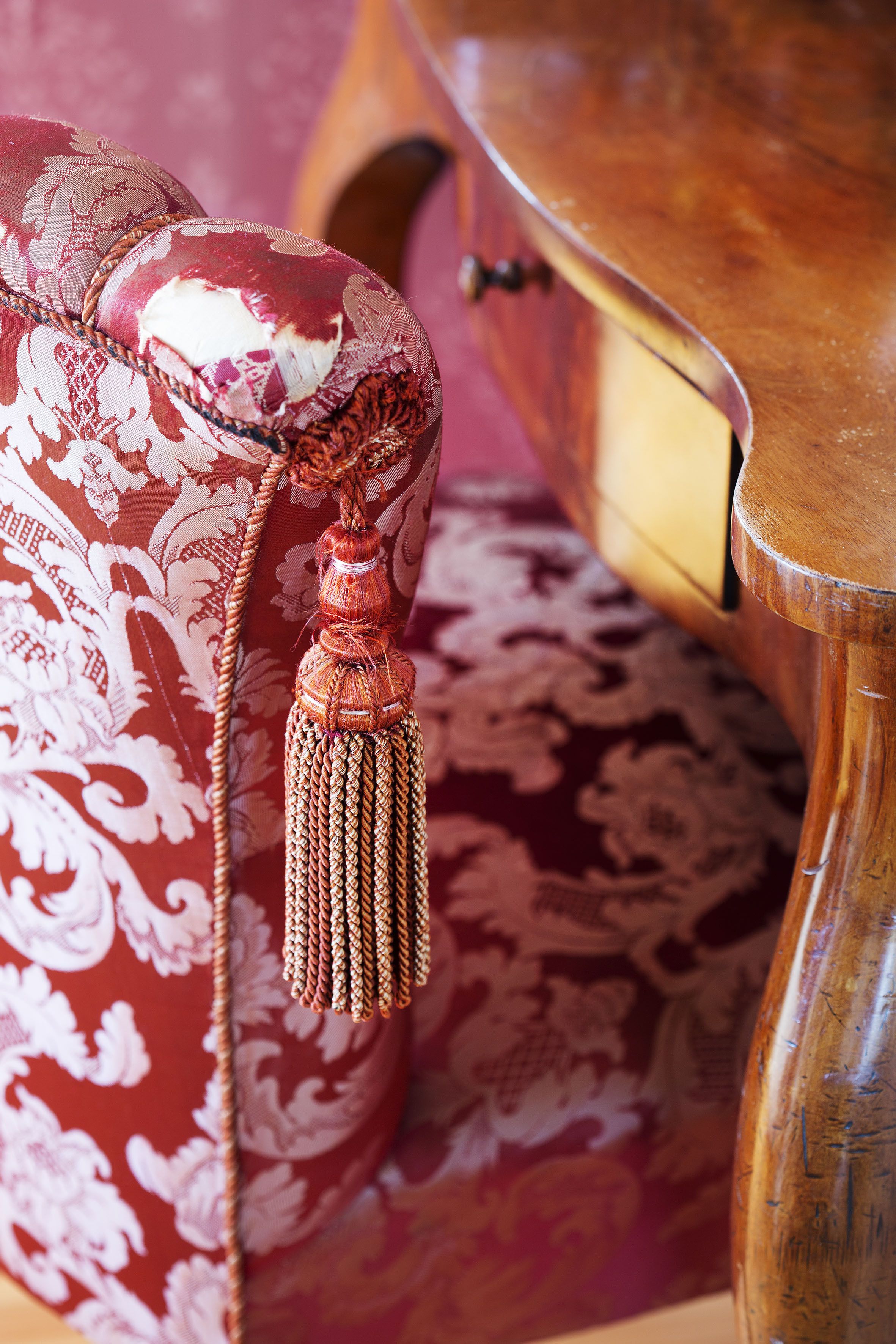 A close-up of a red patterned fabric with a tassel, part of a piece of furniture.