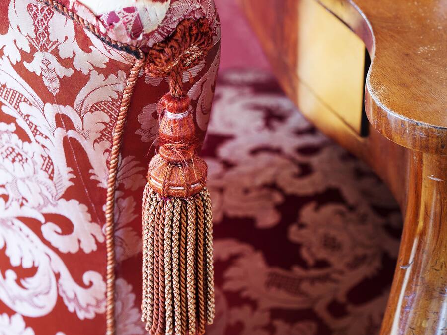 A close-up of a red patterned fabric with a tassel, part of a piece of furniture.