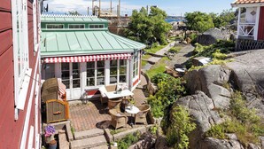 A covered outdoor seating area with wicker furniture and a view of a rocky garden. - Strandflickornas Havshotell (Lysekil)