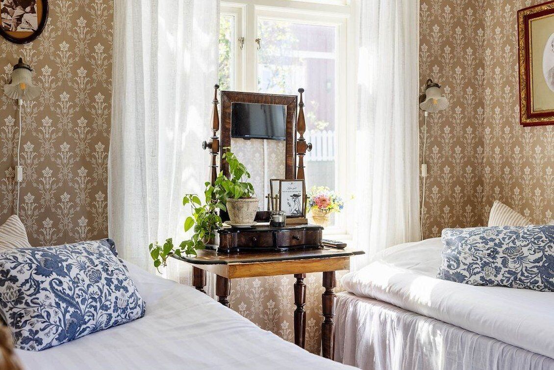 A bedroom with two beds, a wooden table with a mirror, a potted plant, and a wall-mounted TV.