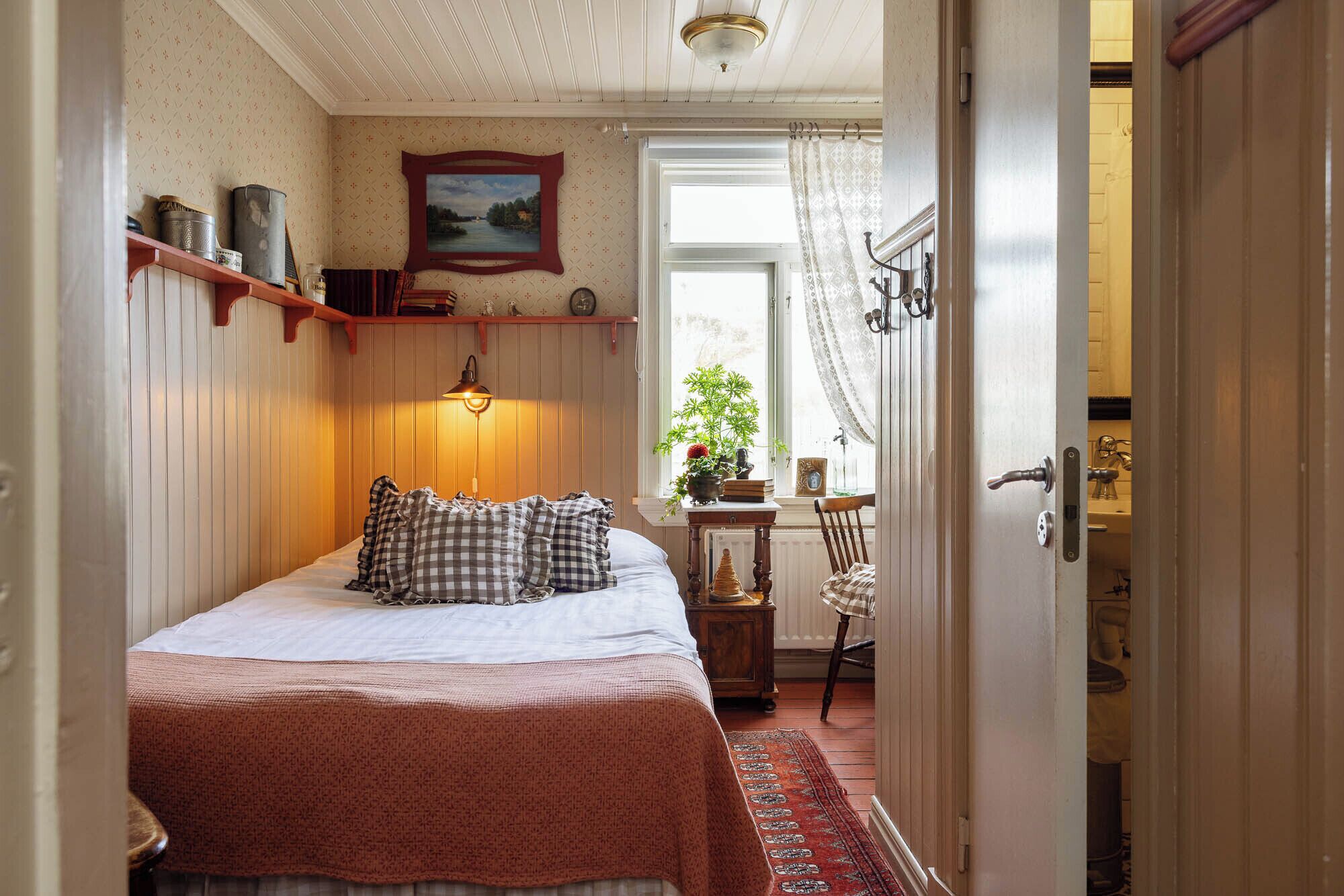 Een slaapkamer met een bed, nachtkastje, raam met uitzicht en een deur naar een andere kamer.
