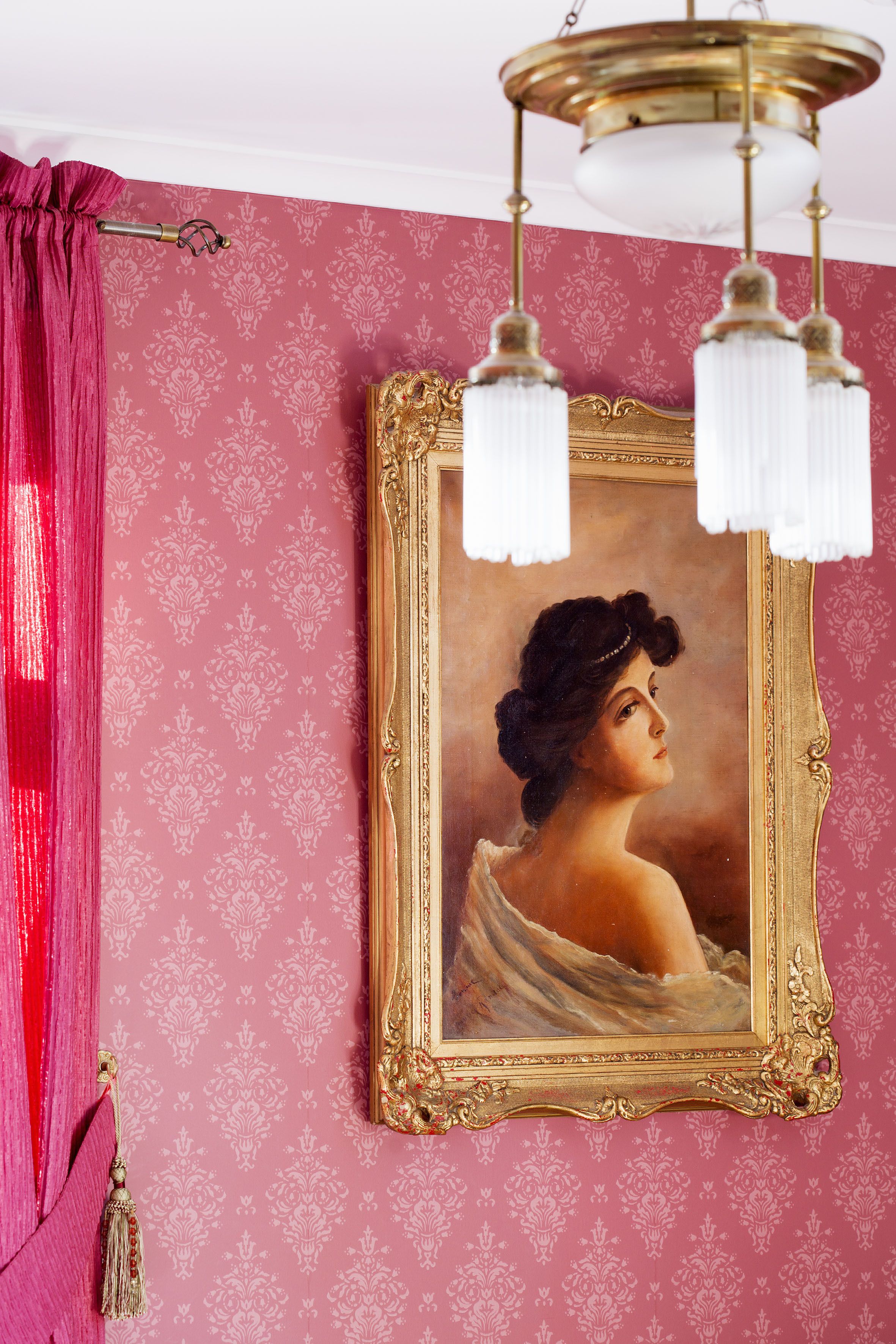 A room with a framed portrait, a chandelier, and a red curtain.