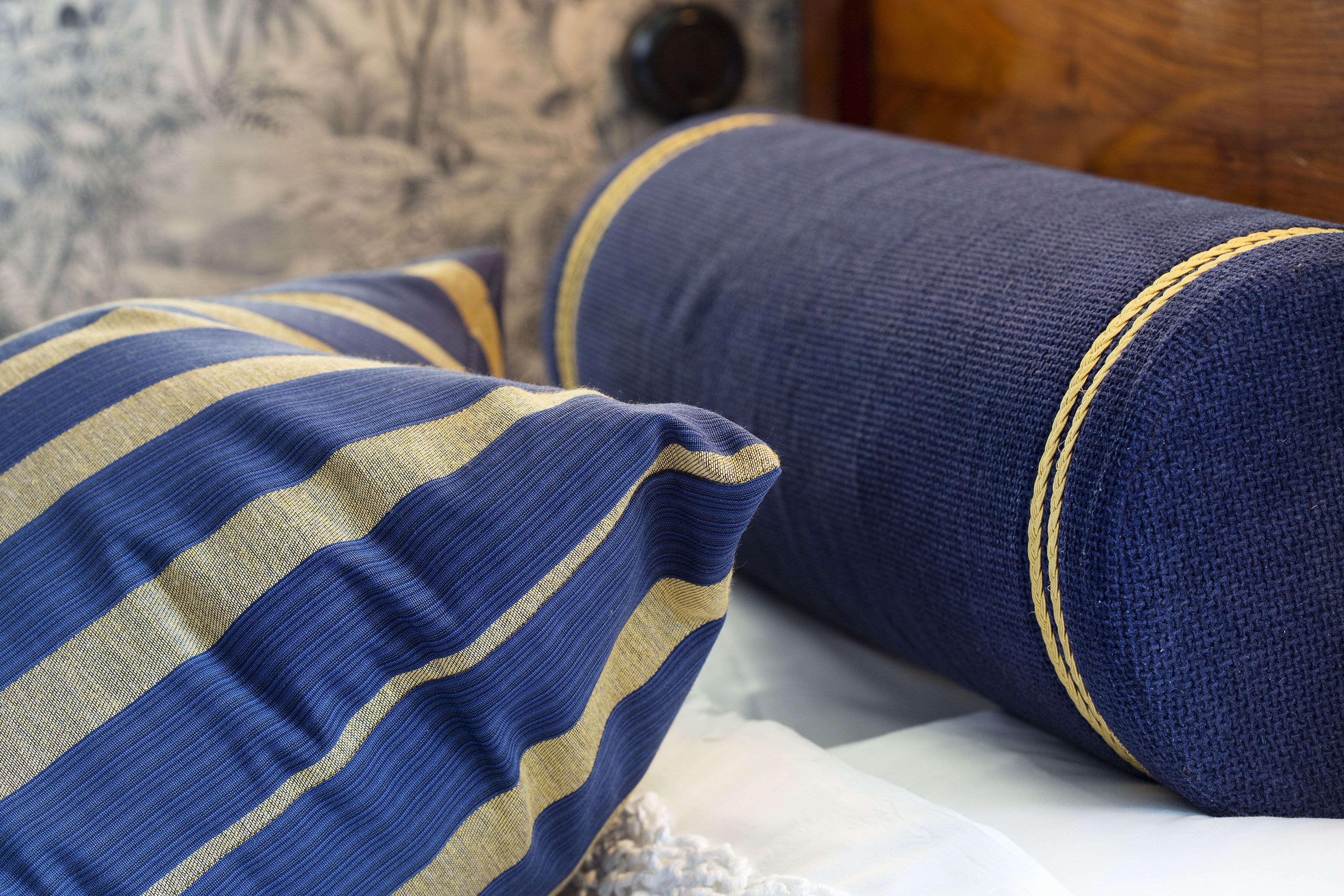 Una cama con un almohadón azul y amarillo a rayas y un almohadón azul liso con costuras amarillas.