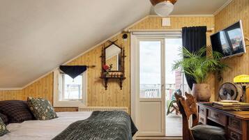 A cozy attic bedroom with a sloped ceiling, a large bed, a desk with a chair, a television, and a potted plant.