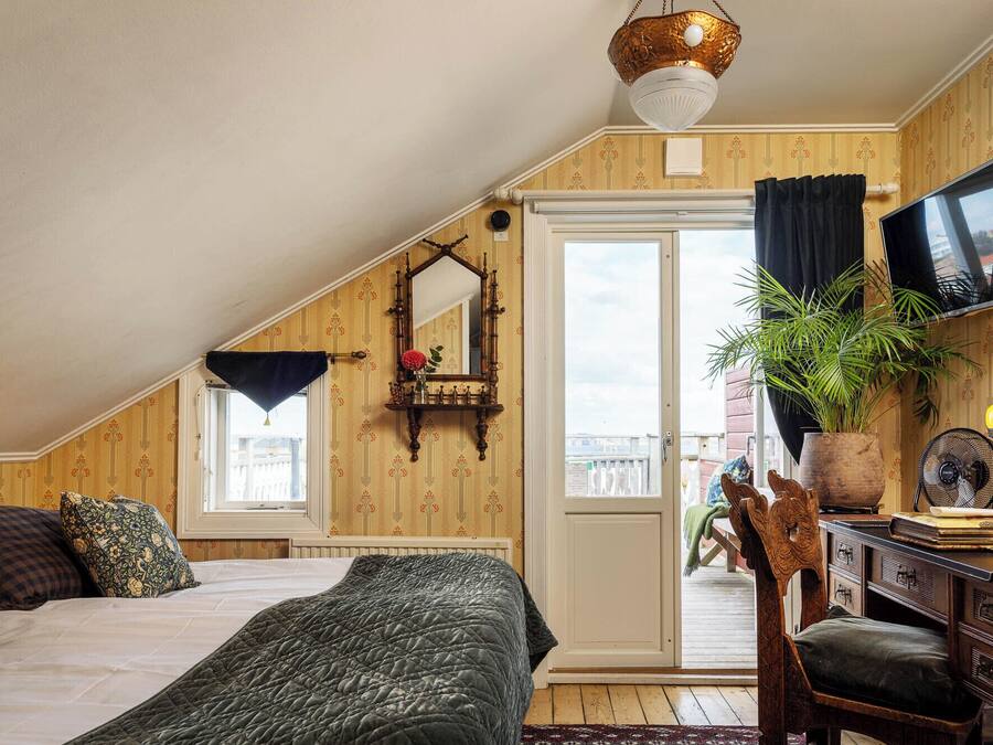 A cozy attic bedroom with a sloped ceiling, a large bed, a desk with a chair, a television, and a potted plant.