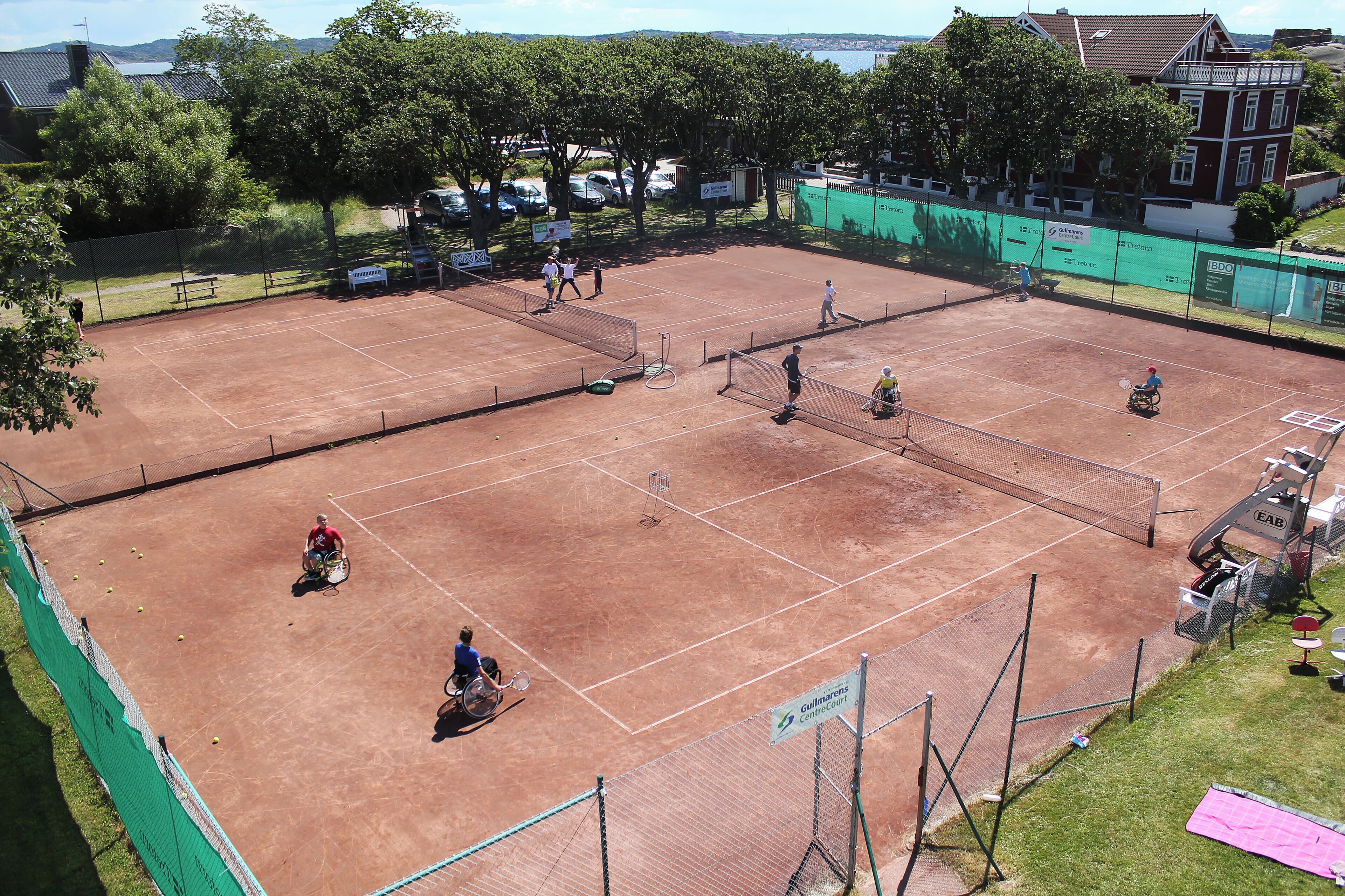 Ein Tennisplatz mit Netz, einem Rollstuhl und einer Bank.