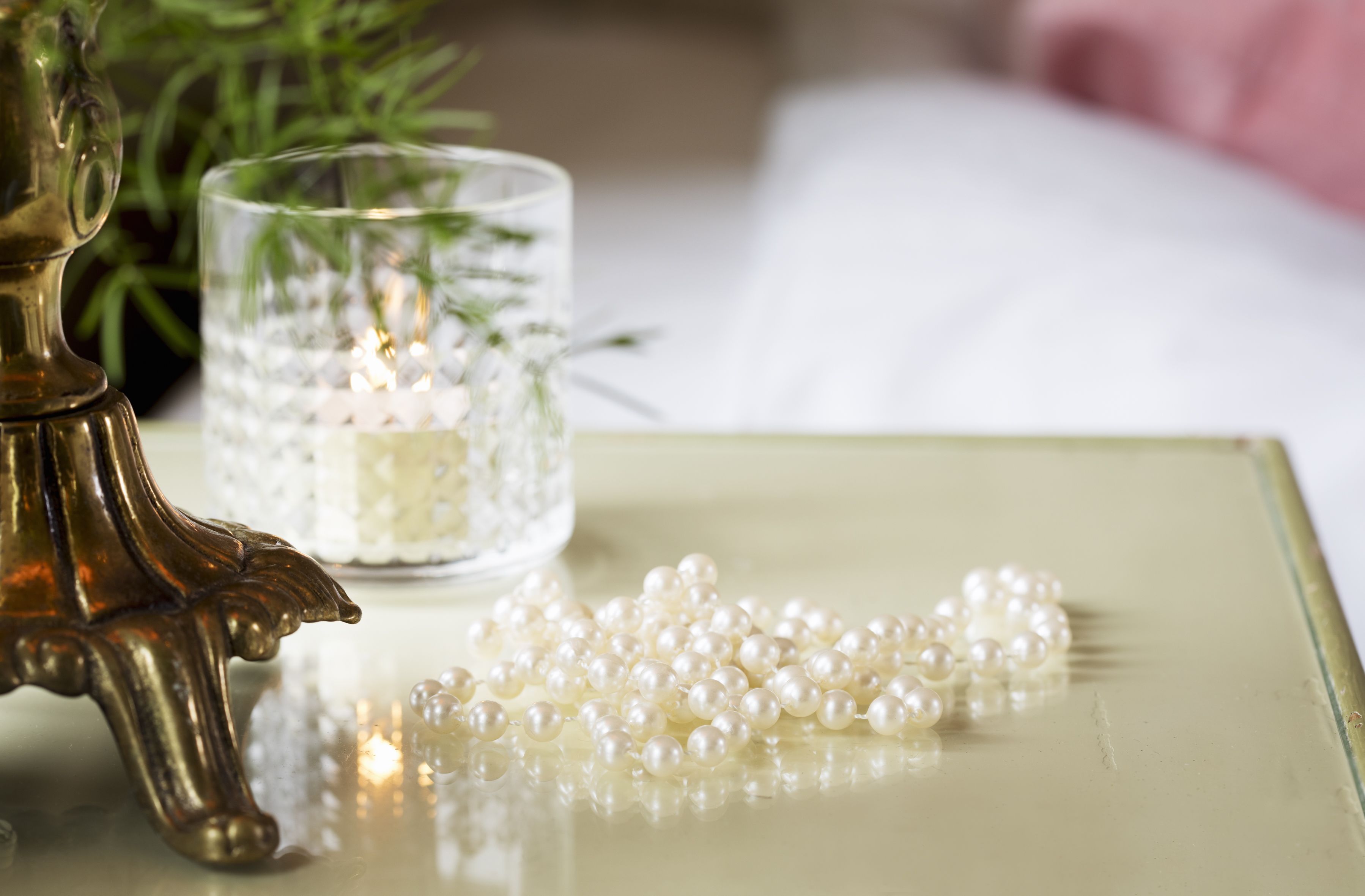 A decorative table with a clear glass candle holder, a brass candle holder, and scattered pearls.