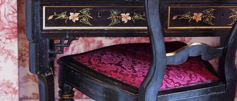 A vintage wooden desk with intricate floral carvings and a cushioned chair with a patterned fabric.