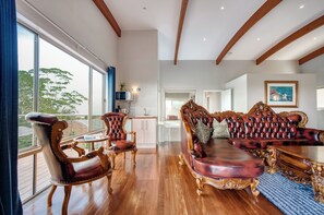 A spacious room with a large window, a wooden ceiling, and a plush red leather sofa. - Maleny Terrace Cottages (Maleny)