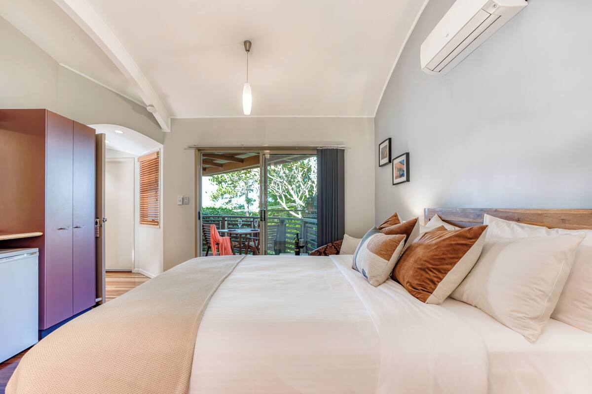 A bedroom with a large bed, a wardrobe, a ceiling fan, and a view of the outdoors.