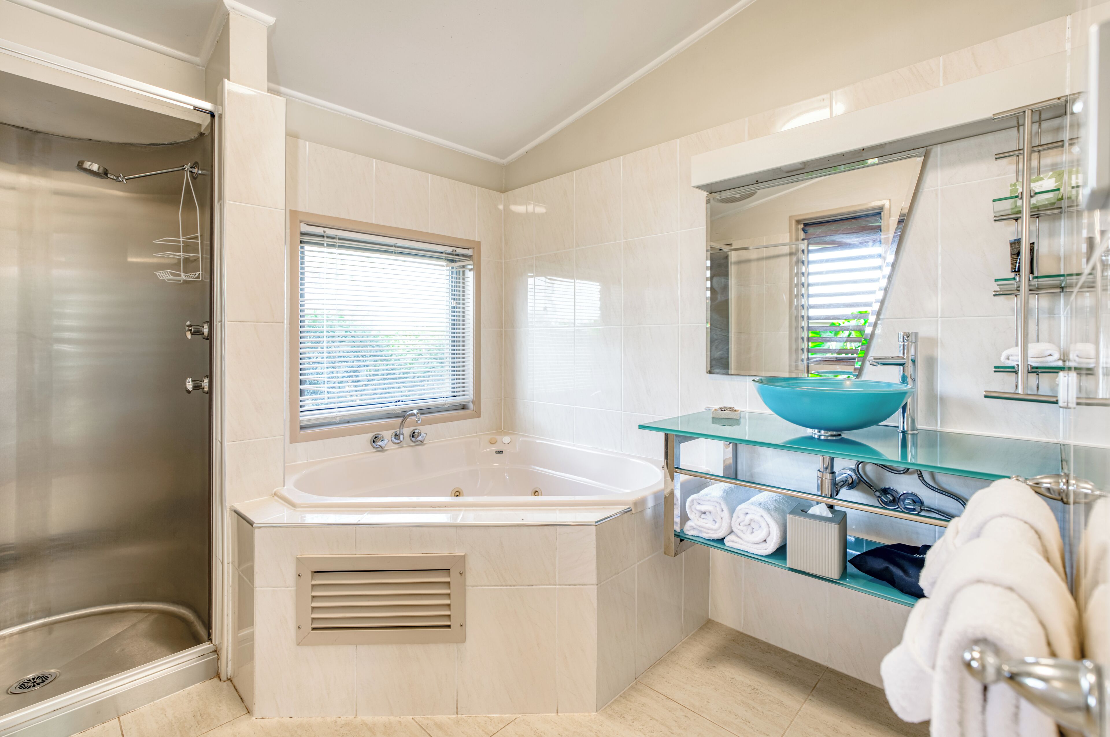 A modern bathroom with a glass-enclosed bathtub, a large mirror, and a glass shelf with toiletries.