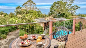 Une table à manger avec des aliments pour le petit-déjeuner, une chaise et une vue sur un jardin luxuriant et des bâtiments éloignés.