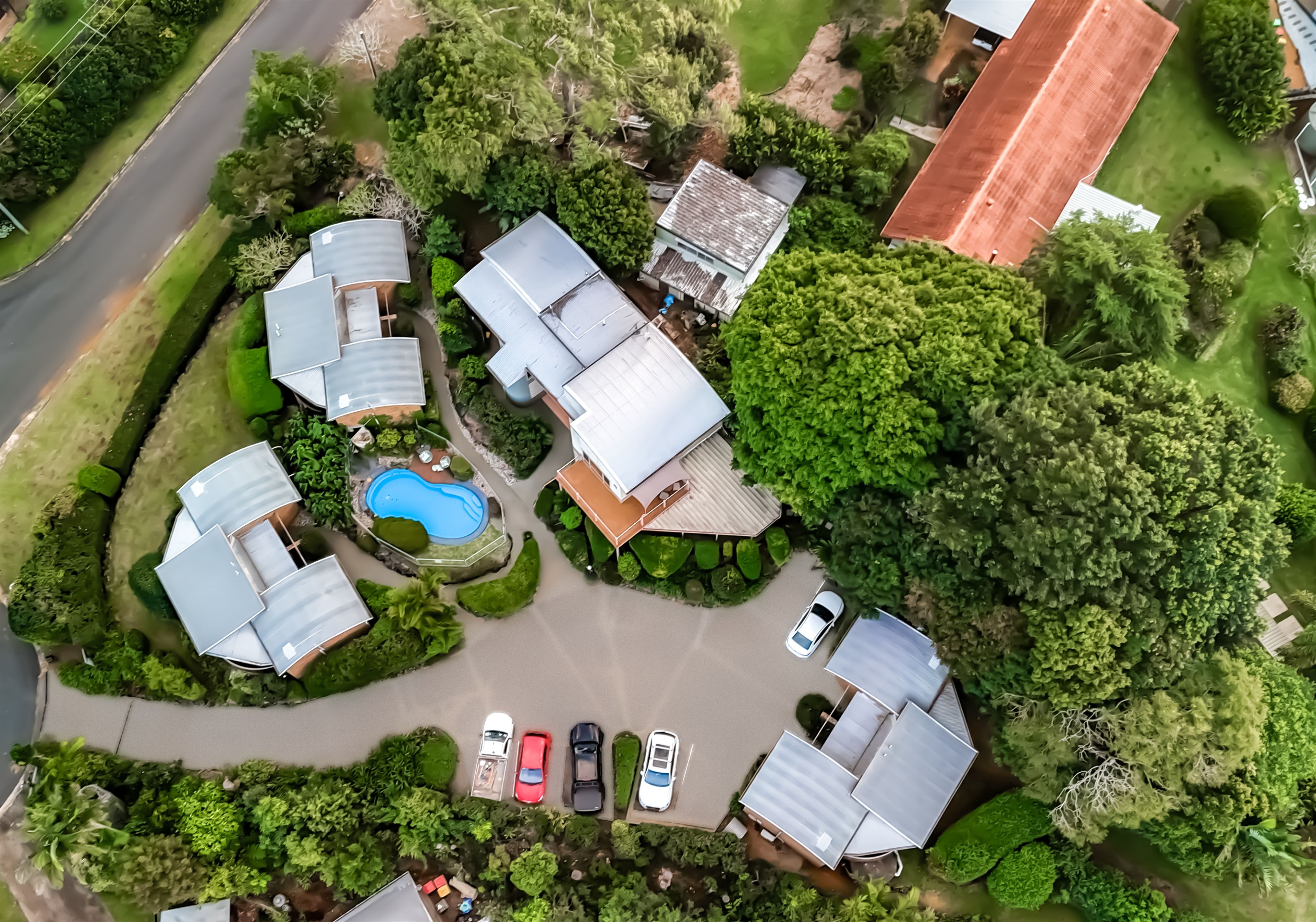 A residential area with multiple houses, a swimming pool, and a parking lot with several cars.