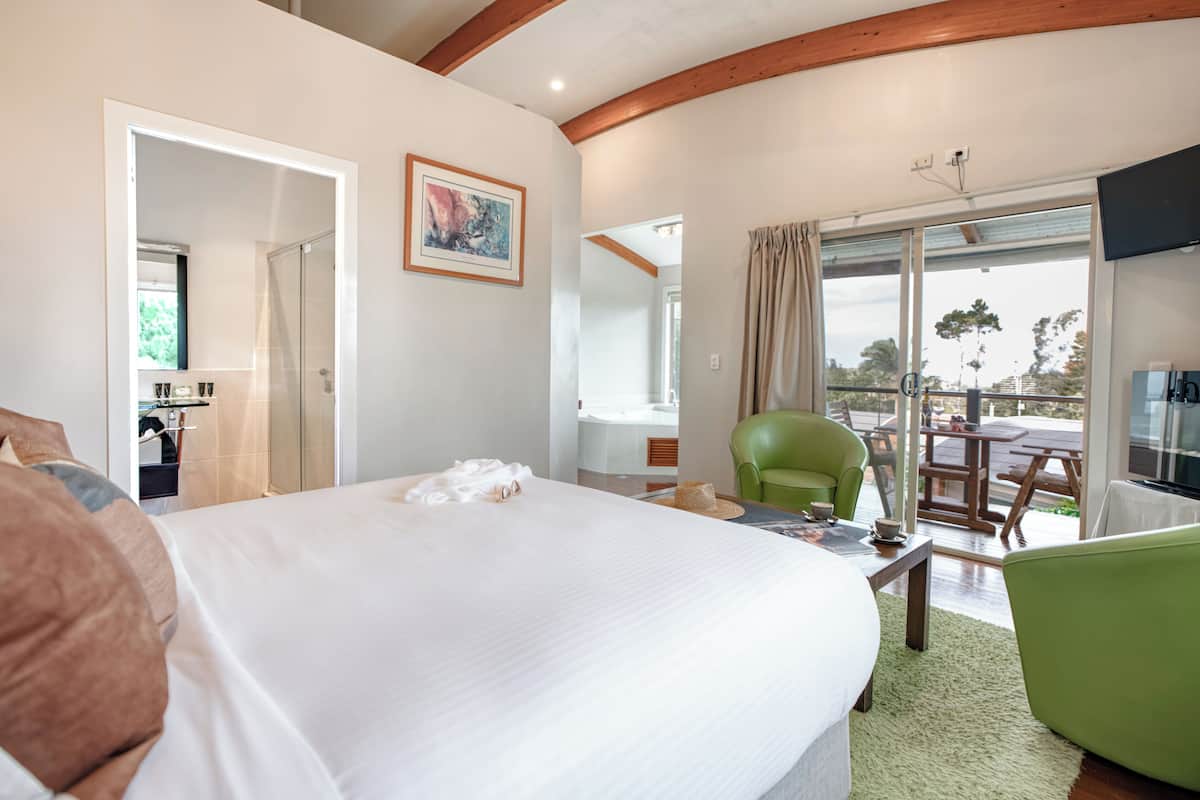 A hotel room with a bed, a green chair, a dining table, and a view of the outdoors.