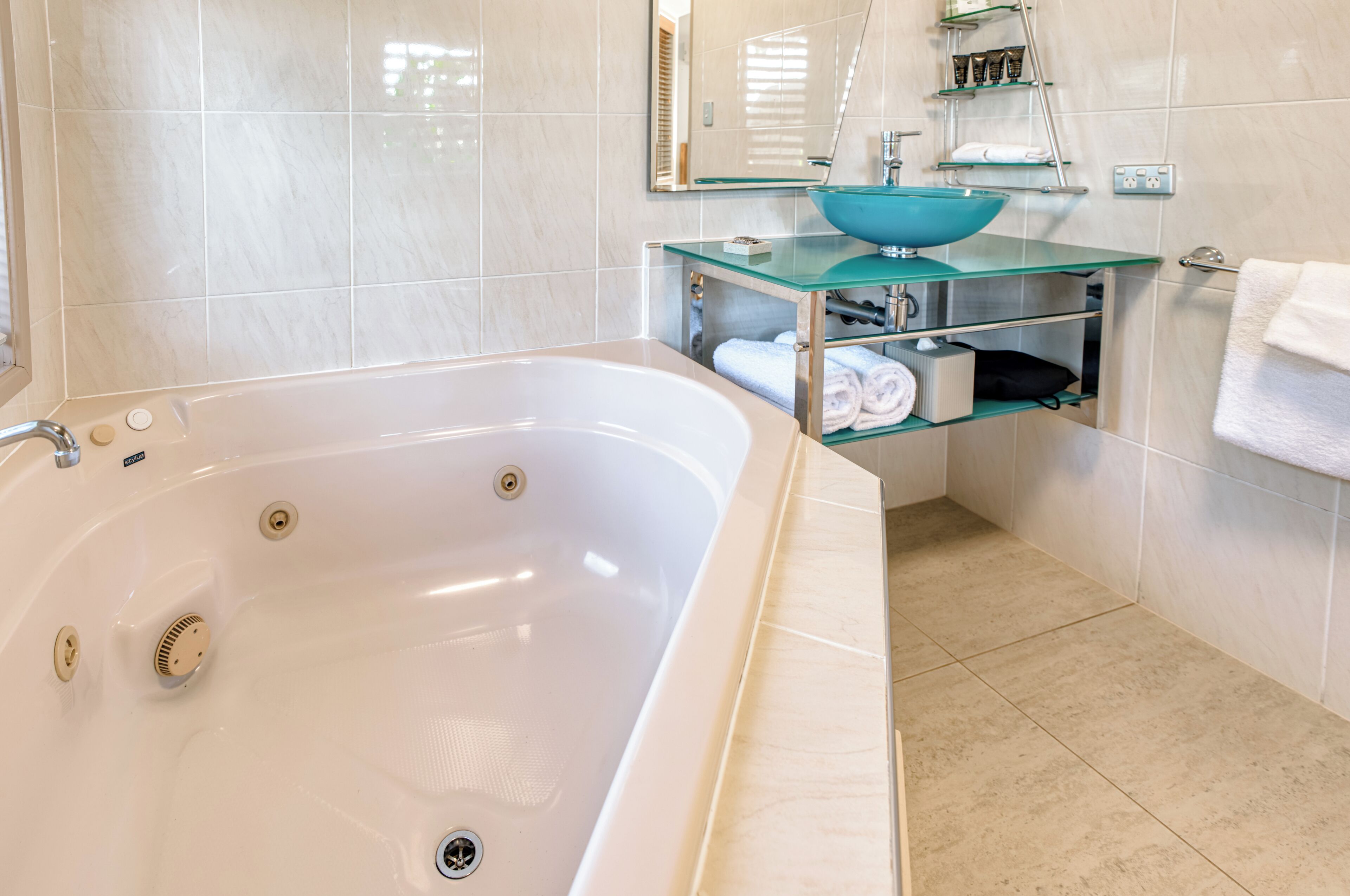A modern bathroom with a large bathtub, a glass sink, and a built-in shelf with towels.
