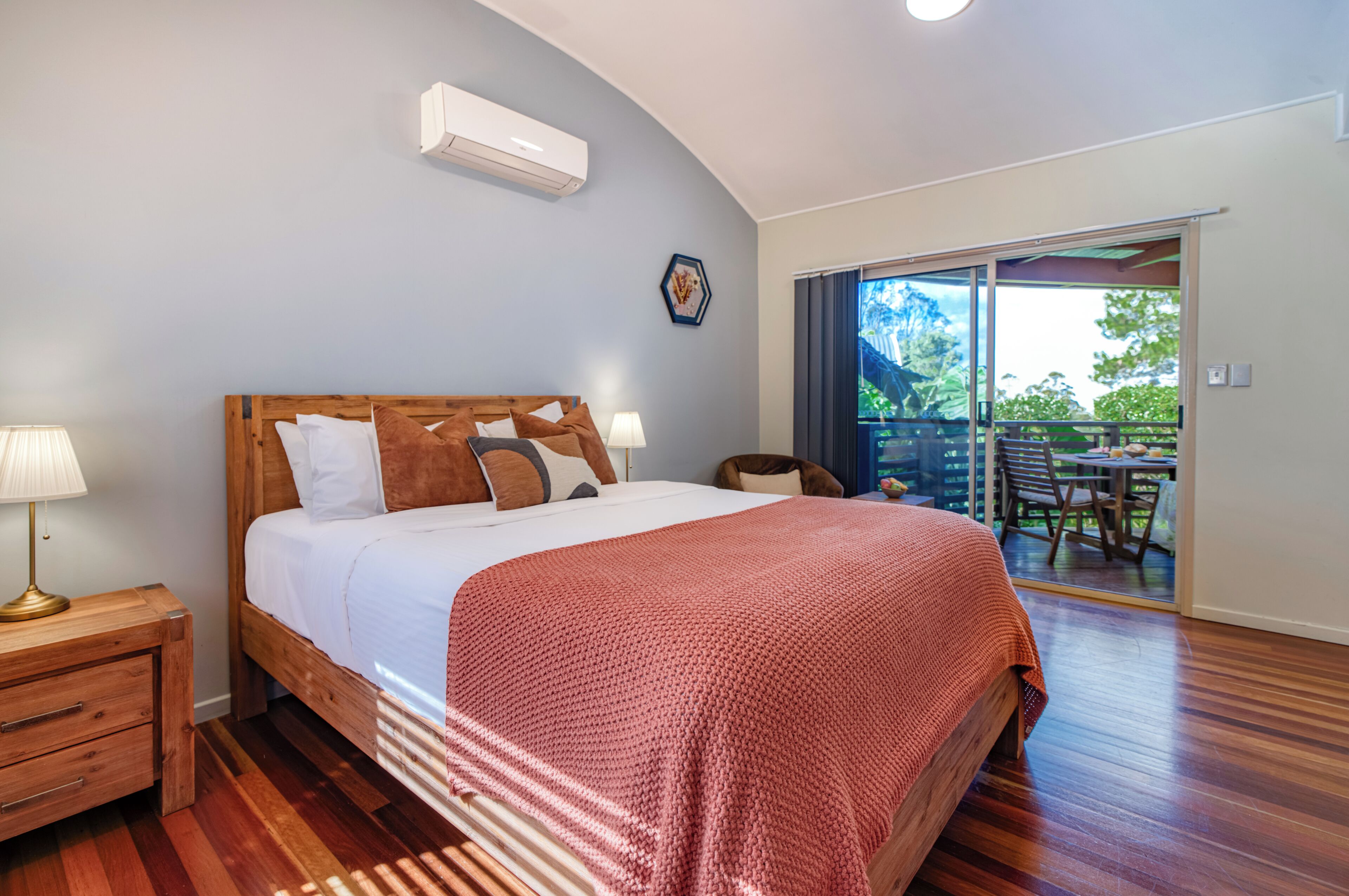 A bedroom with a wooden bed, a nightstand, a lamp, and a view of an outdoor patio.
