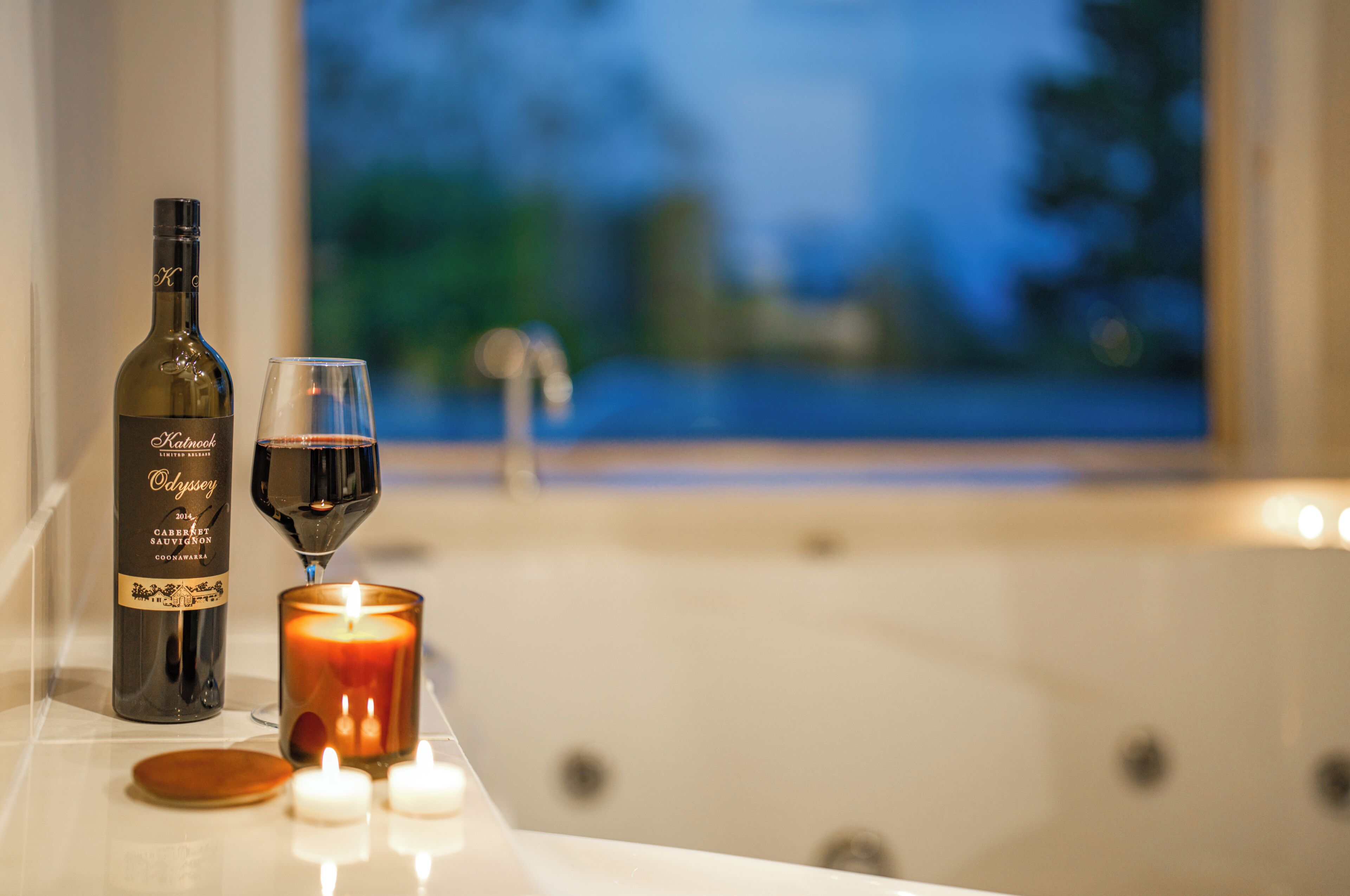 Une bouteille de vin, un verre de vin rouge, une bougie allumée et une baignoire dans une pièce avec vue.