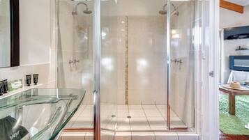 A glass-enclosed shower area with a glass partition, a glass countertop with toiletries, and a wooden ceiling beam.