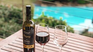 A wooden table with a bottle of wine, two glasses, a bowl of grapes, a bowl of crackers, and a piece of cheese.