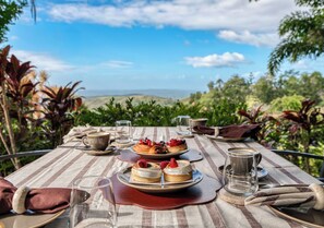 A table set with plates of desserts, glasses, and cutlery, overlooking a scenic landscape. - Maleny Terrace Cottages (Maleny)