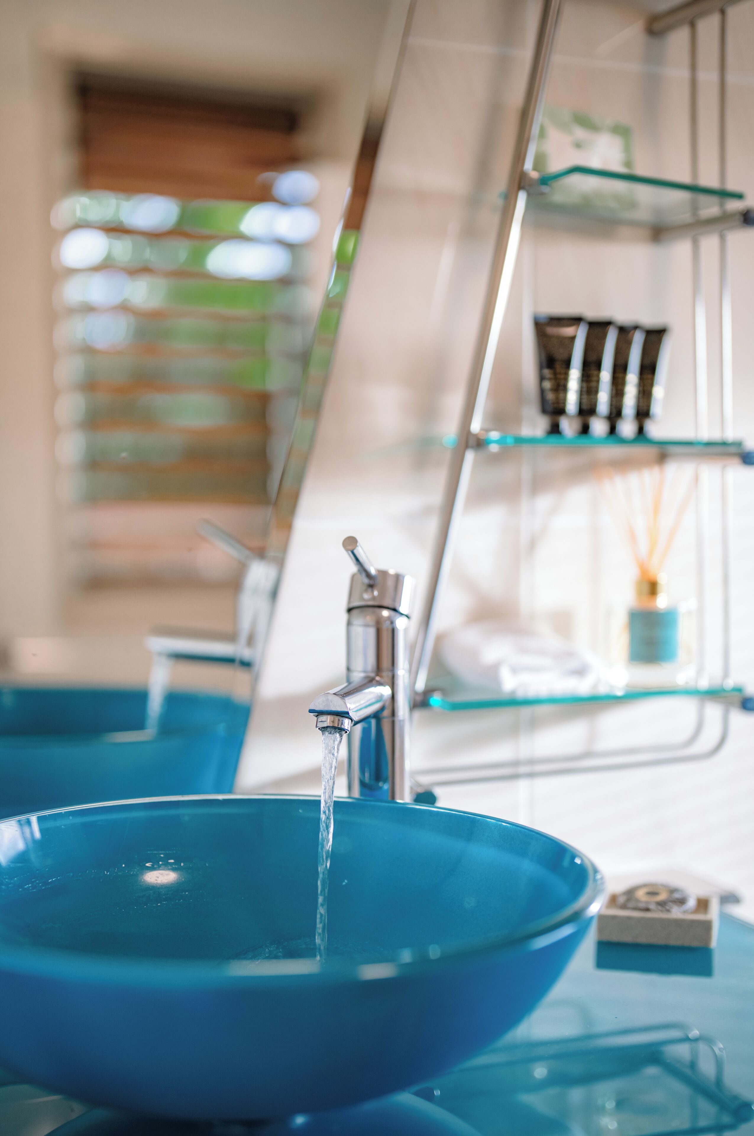 A bathroom with a blue sink, a mirror, and a glass shelf with toiletries.