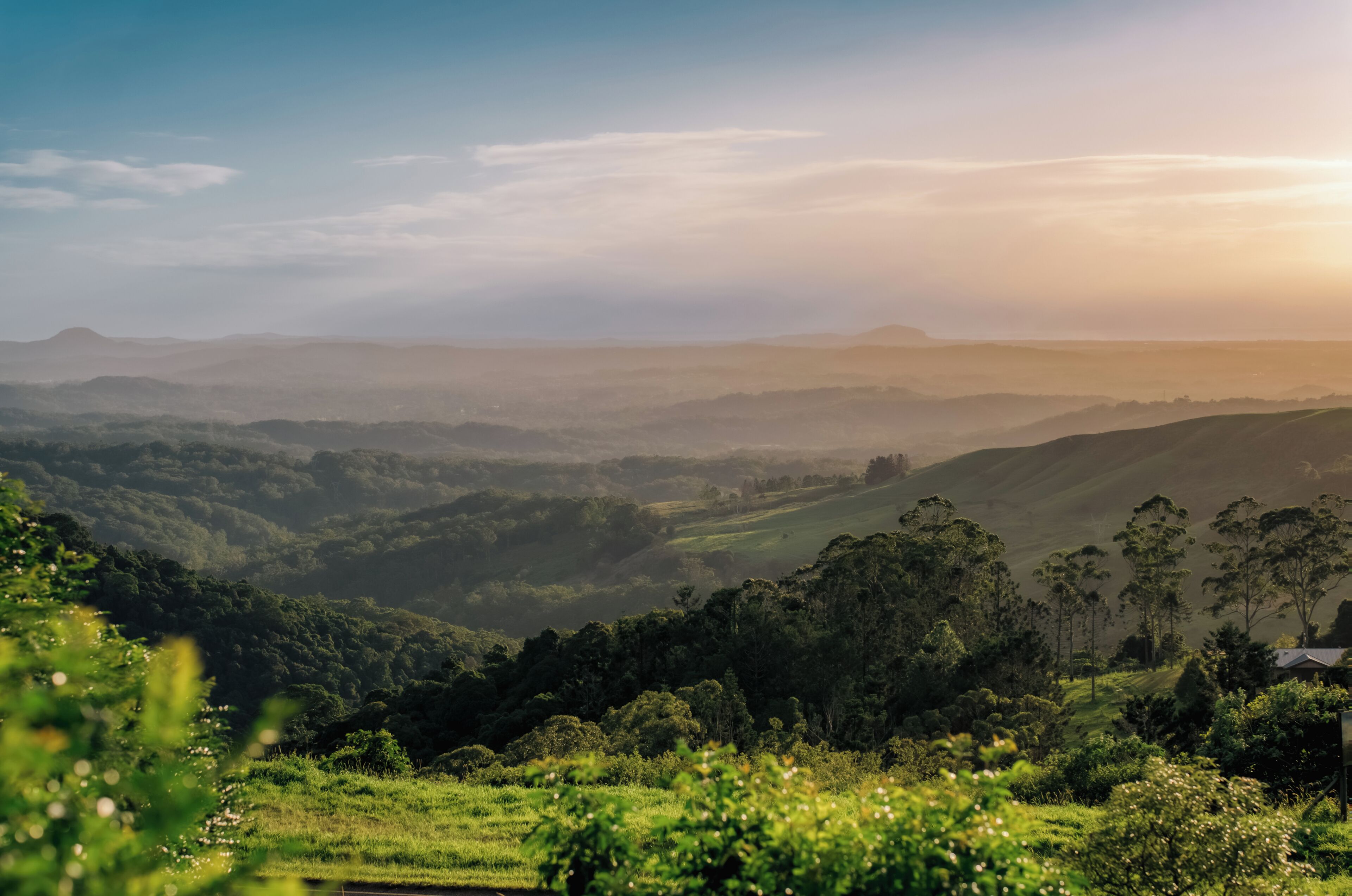 A panoramic view of a lush, green valley with rolling hills and distant mountains under a clear sky.