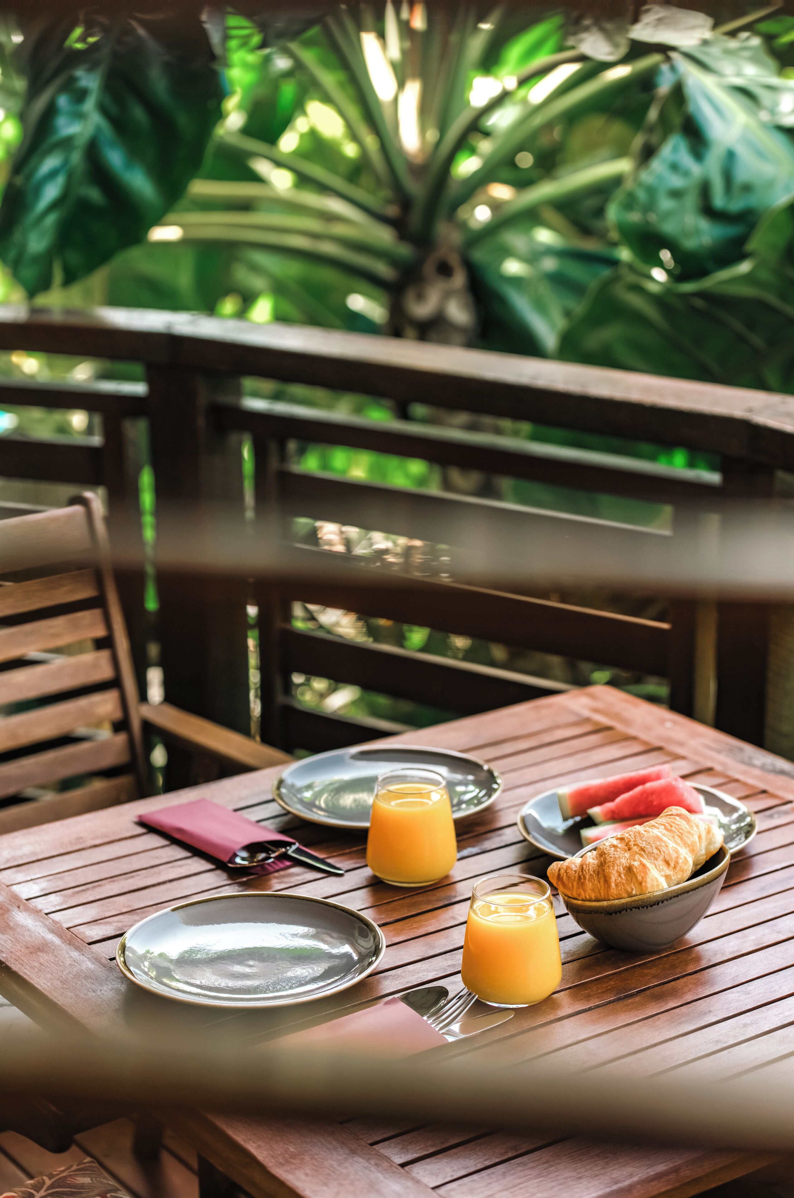 A wooden table with plates, a glass of orange juice, a croissant, and a watermelon.