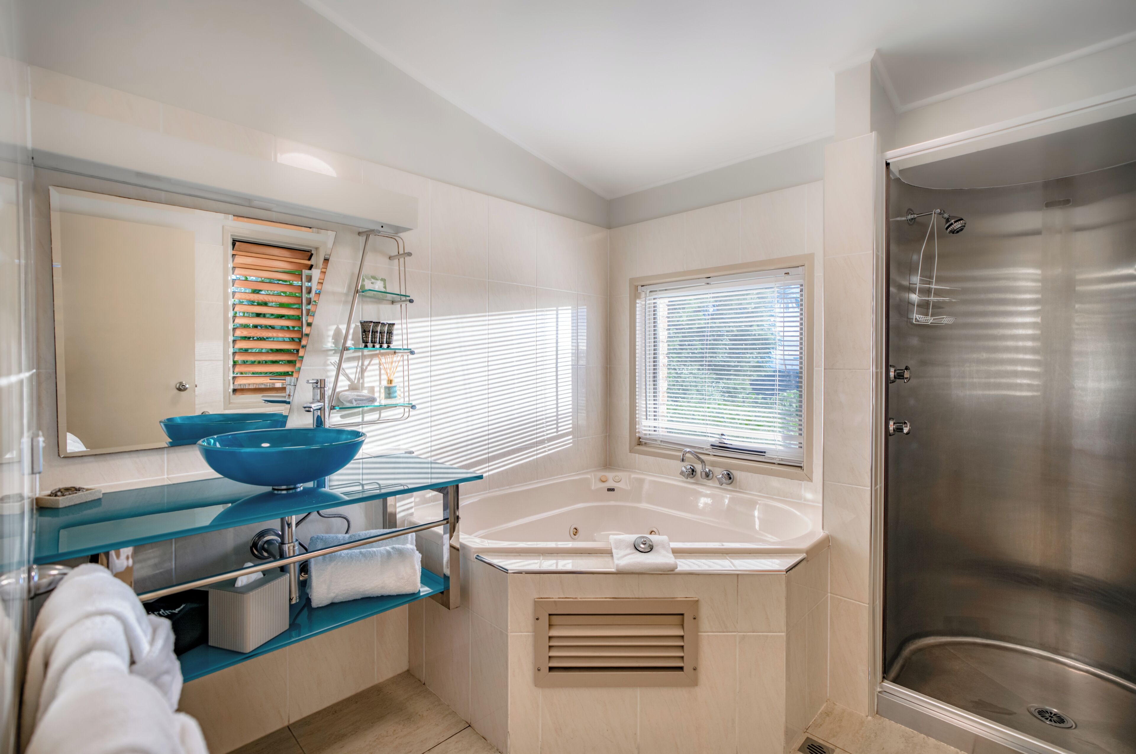 A modern bathroom with a glass sink, a large bathtub, and a shower area.