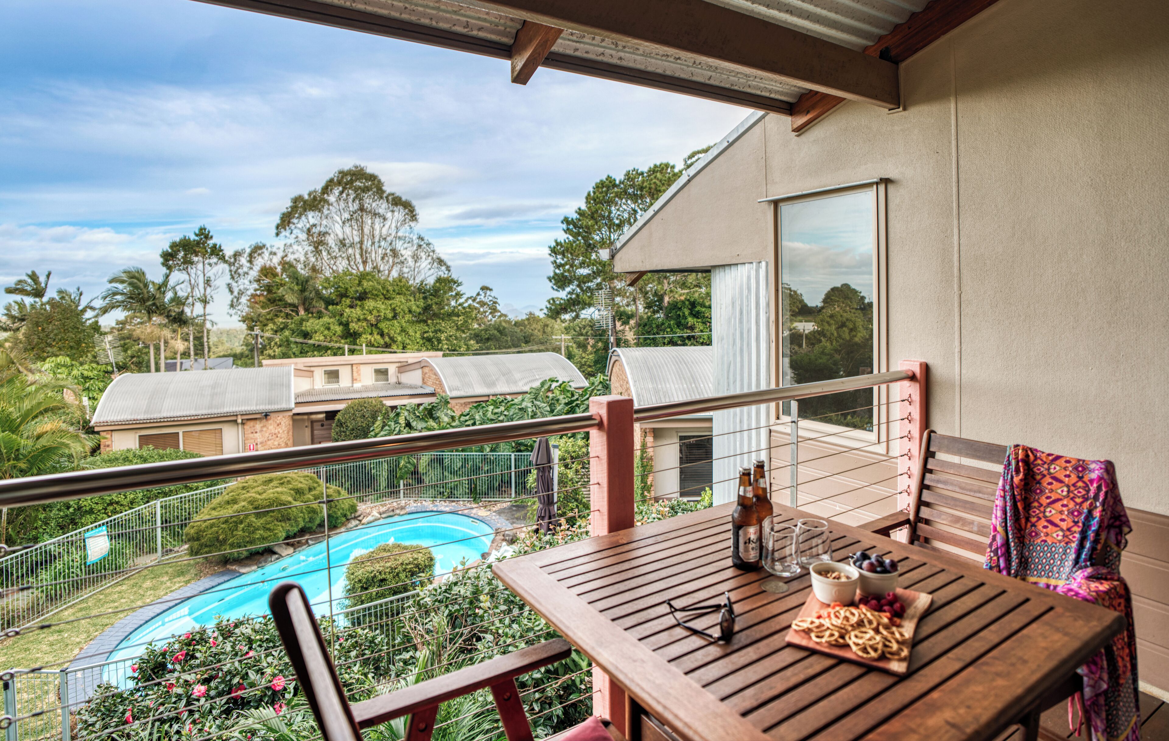 A balcony with a pool, wooden furniture, and a bottle of beer.