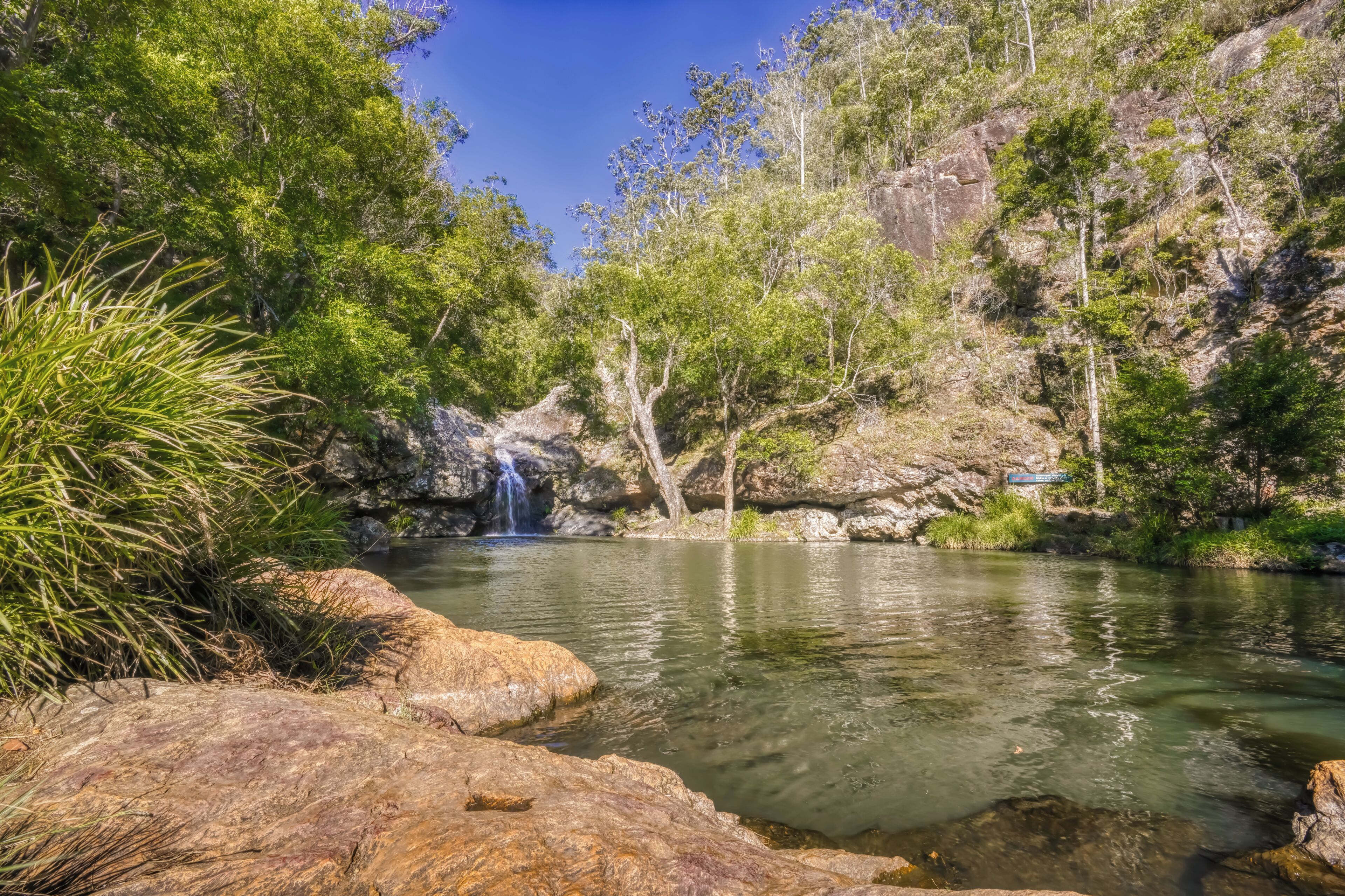 A natural landscape with a clear water body, rocks, and trees.