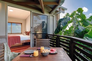 A balcony with a wooden table, breakfast items, and a bed with a red blanket. - Maleny Terrace Cottages (Maleny)