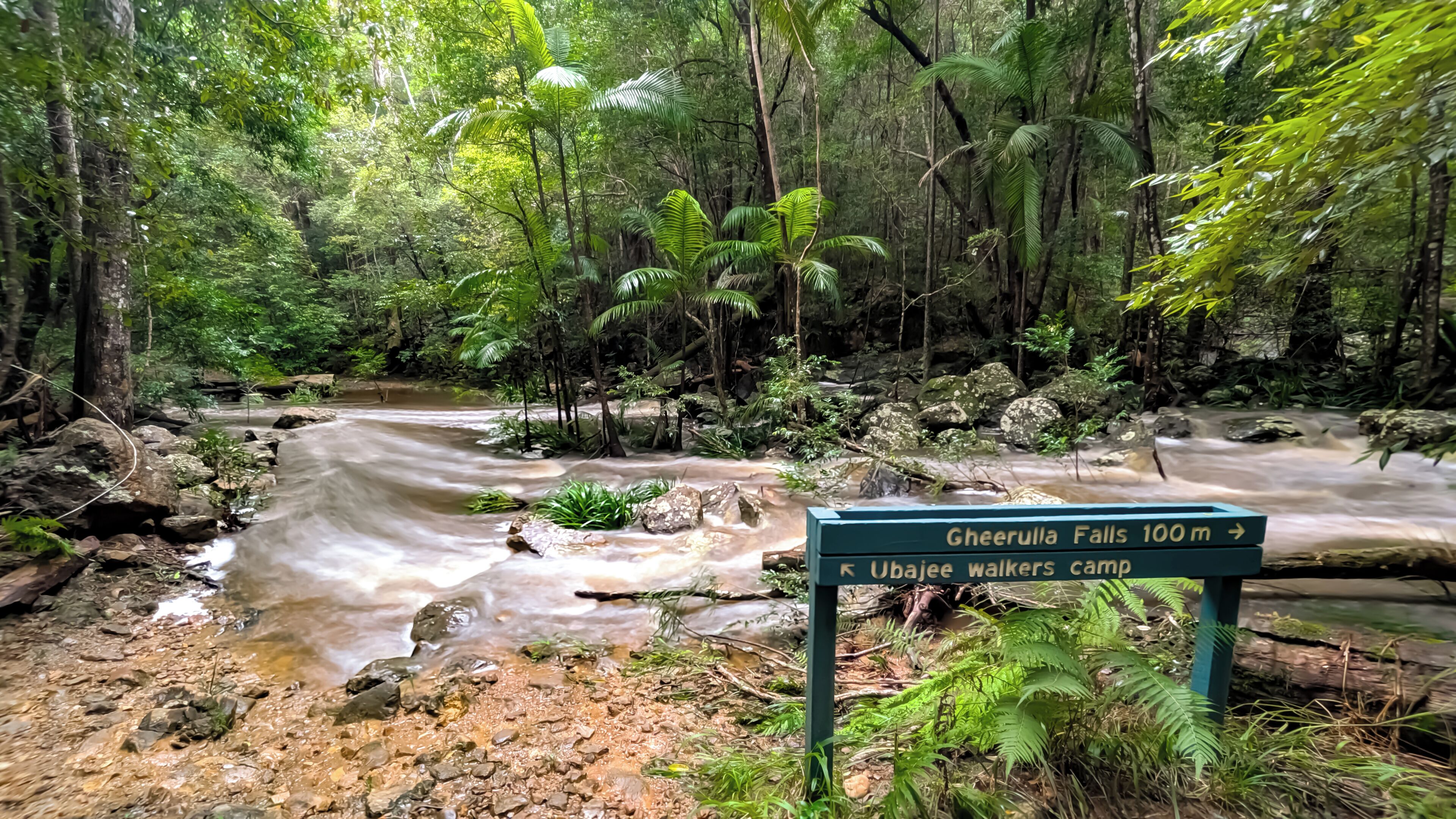 A forested area with a sign indicating directions to Gheerulla Falls and Ujaee walkers camp.