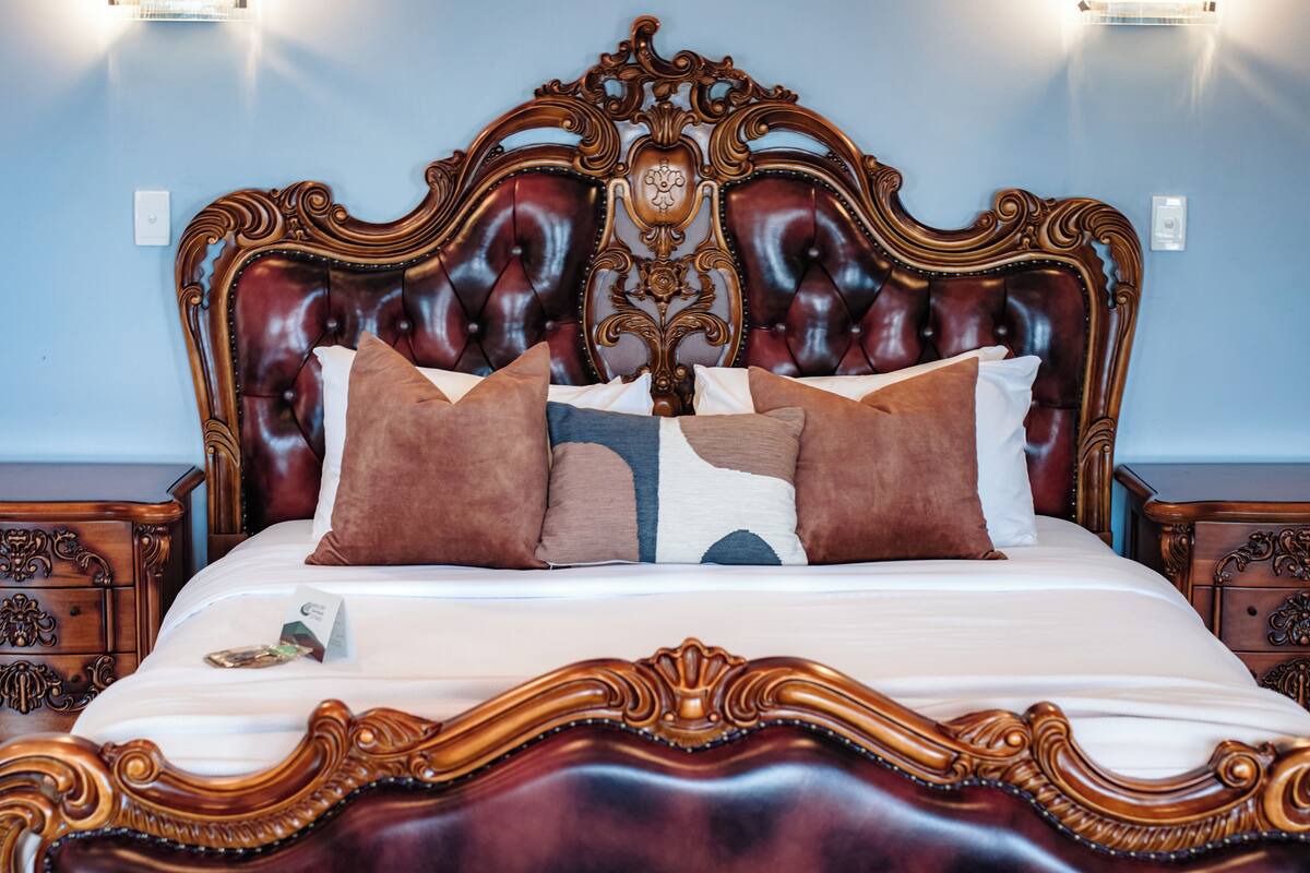 A bed with an ornate headboard, a white mattress, and multiple pillows.