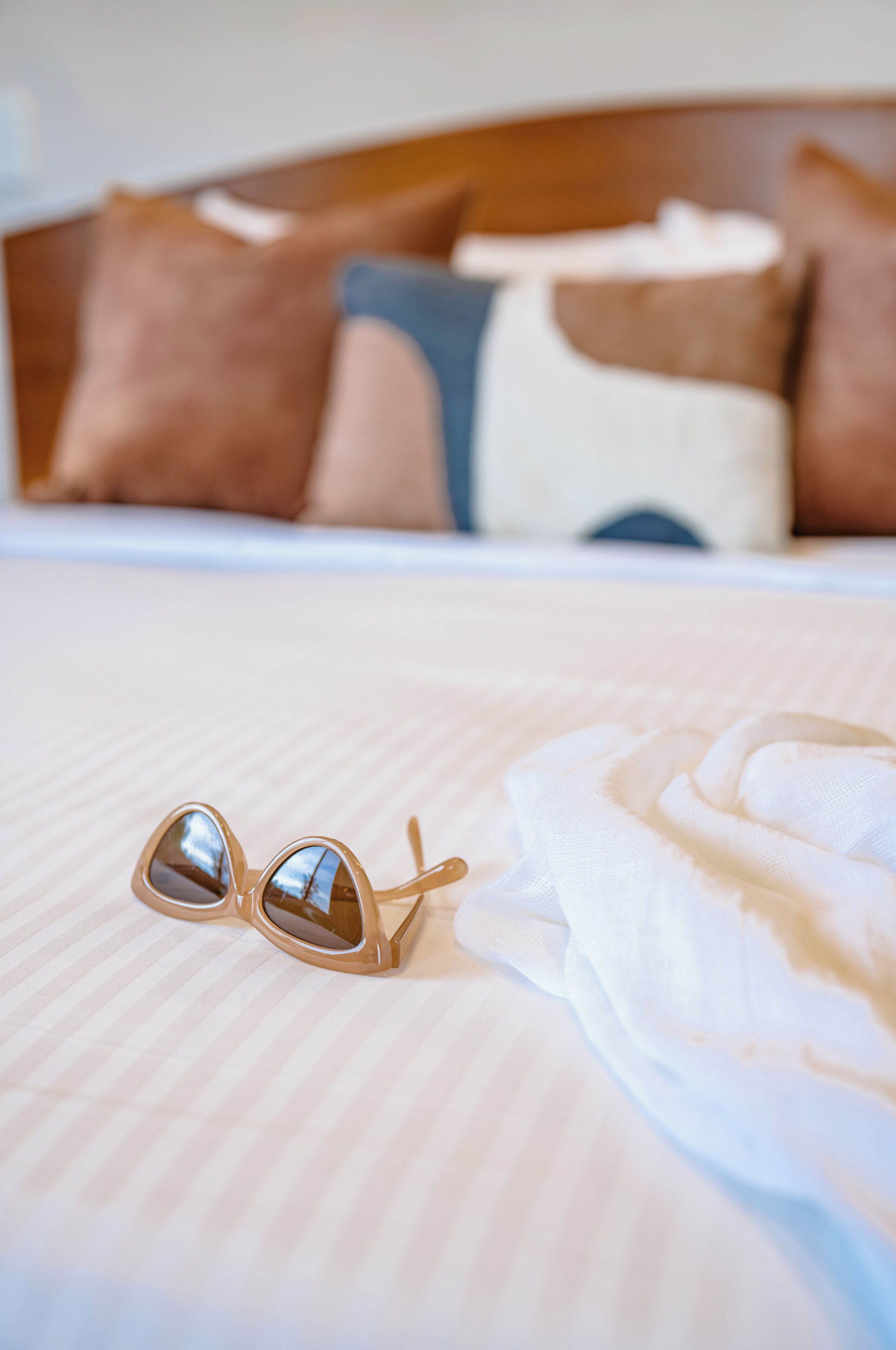 Un lit avec une tête de lit, une paire de lunettes de soleil et un tissu blanc posé sur le lit.