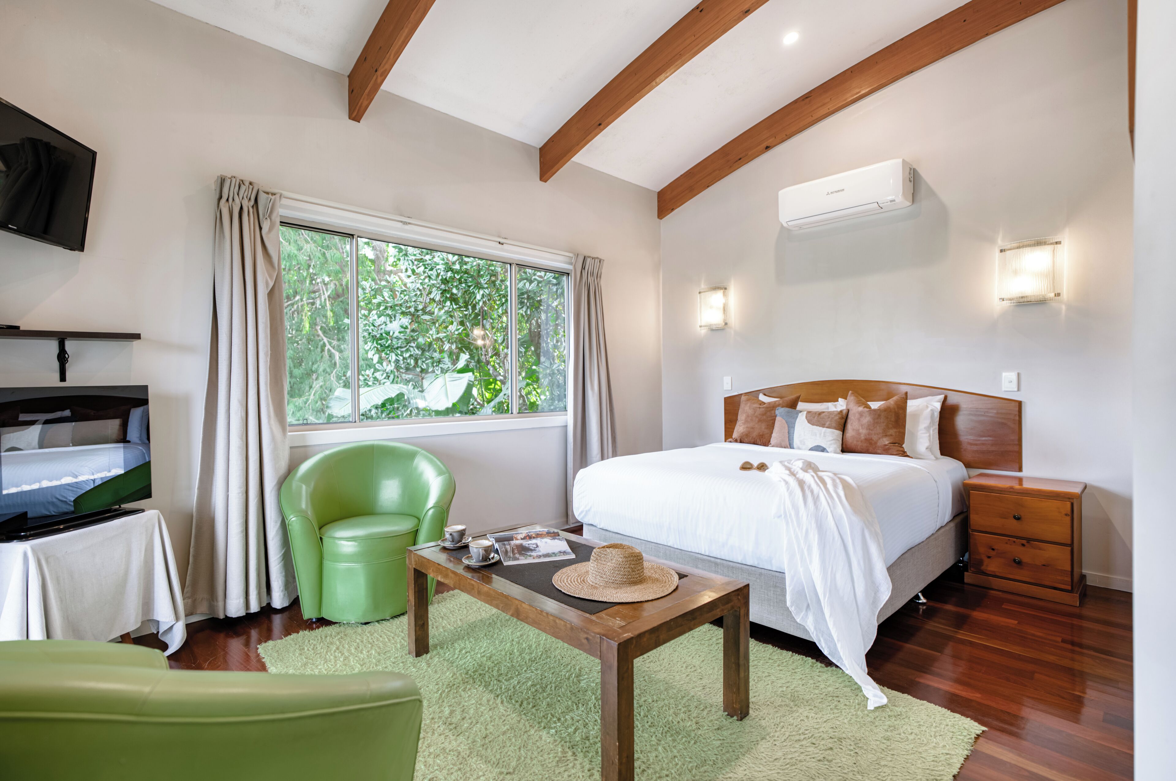 A bedroom with a bed, bedside table, nightstand, TV, and a window with curtains.