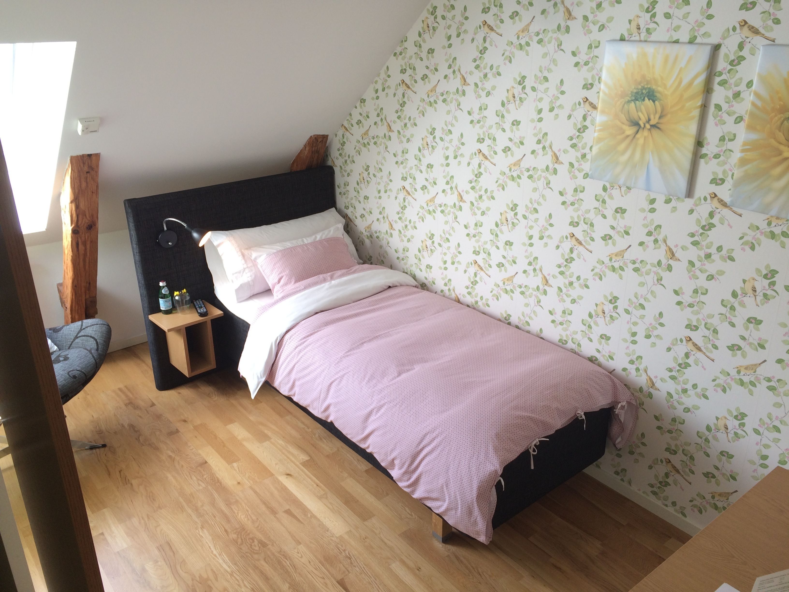 A bedroom with a bed, a nightstand, a chair, and a wall with floral wallpaper.