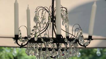 A chandelier with multiple crystal elements and candles, hanging under a structure with a white canopy.
