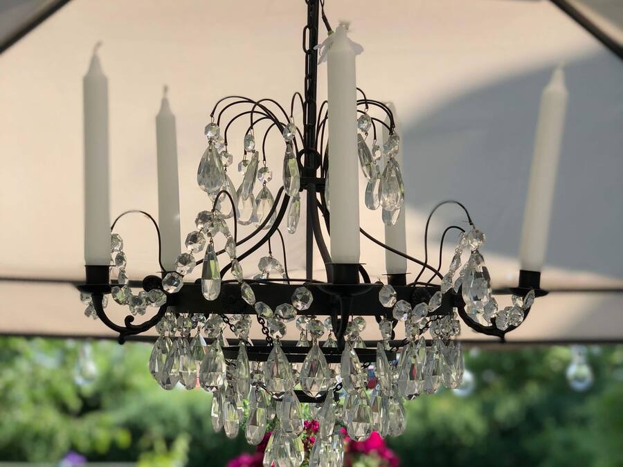 A chandelier with multiple crystal elements and candles, hanging under a structure with a white canopy.