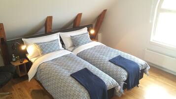 A bedroom with two beds, wooden headboard, bedside lamps, and a window with natural light.
