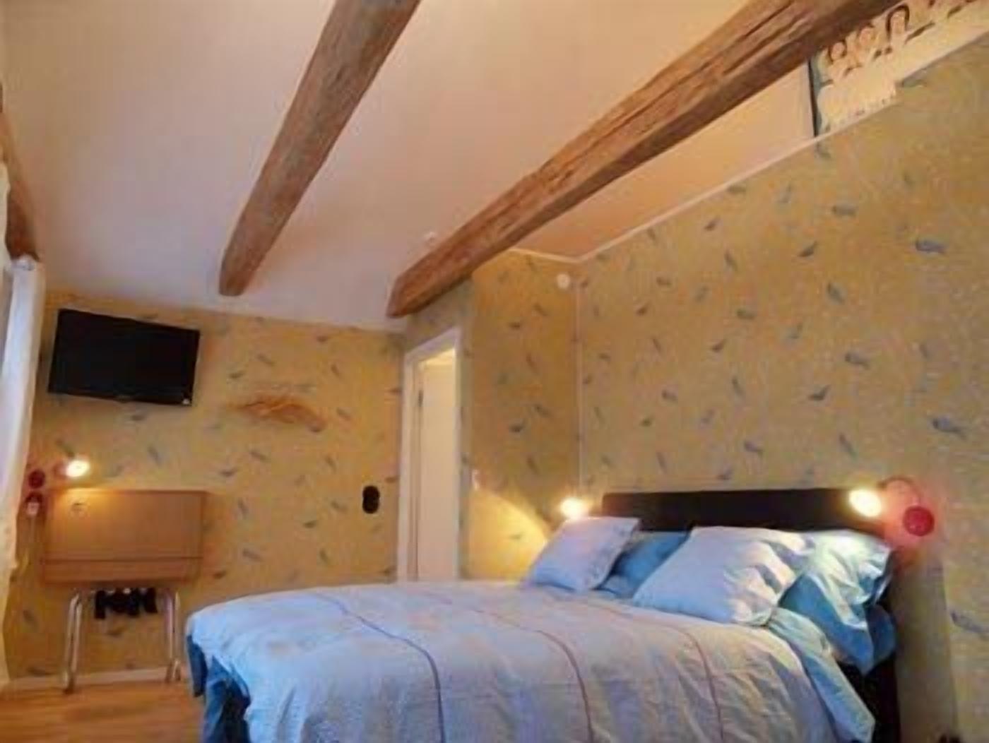 A bedroom with a bed, a television on the wall, and a wooden ceiling beam.