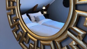 A bedroom with a large, ornate gold-framed mirror reflecting a bed with white linens and a nightstand with a lamp. - Annas Hotell (Kristianstad)