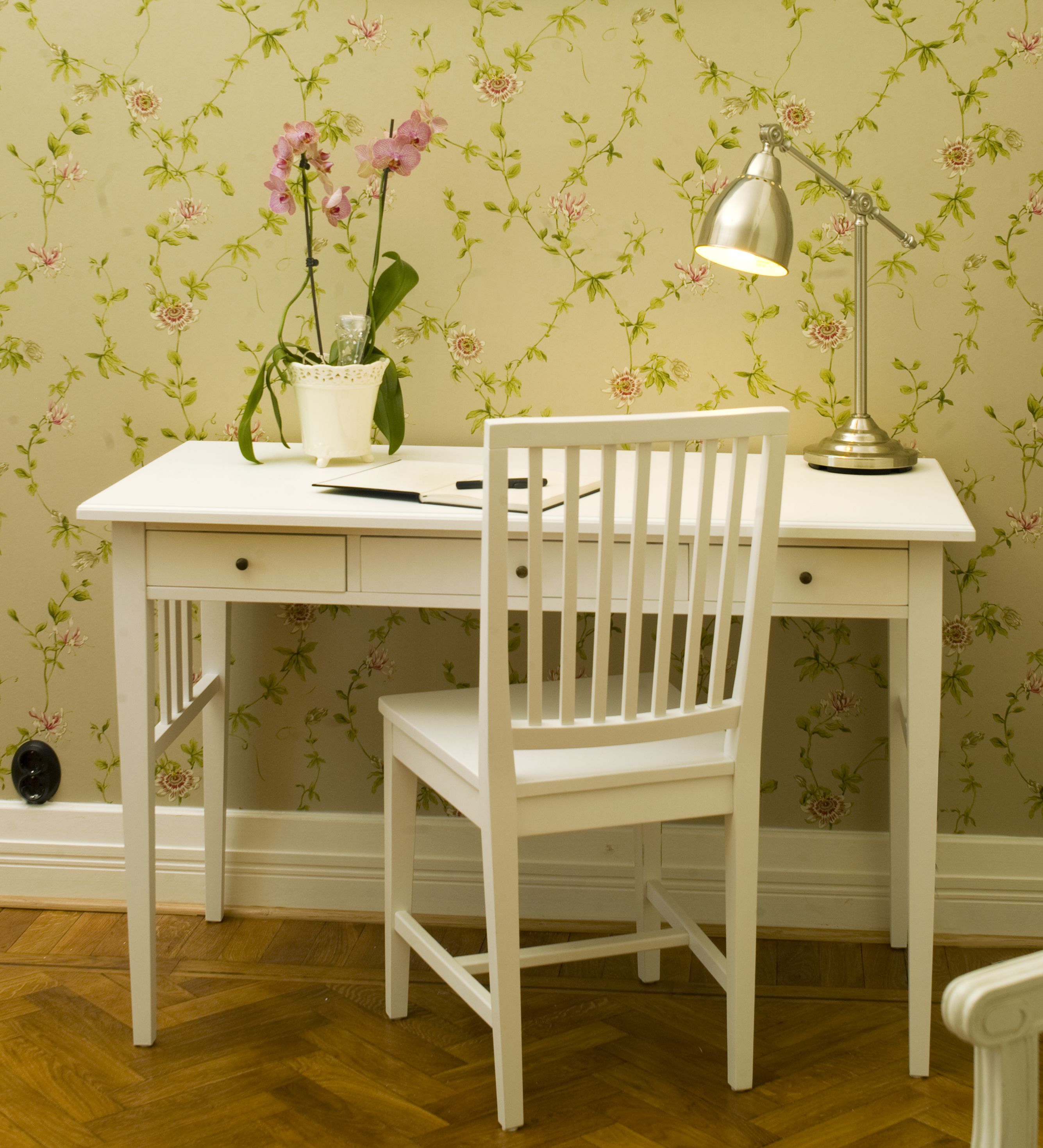 Een wit bureau met een stoel, een lamp en een bloeiende kamerplant.