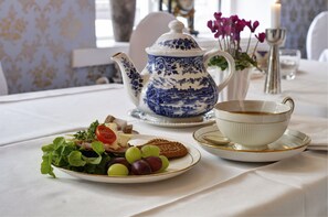 Una mesa dispuesta con tetera, taza, plato con comida y un jarrón con flores.