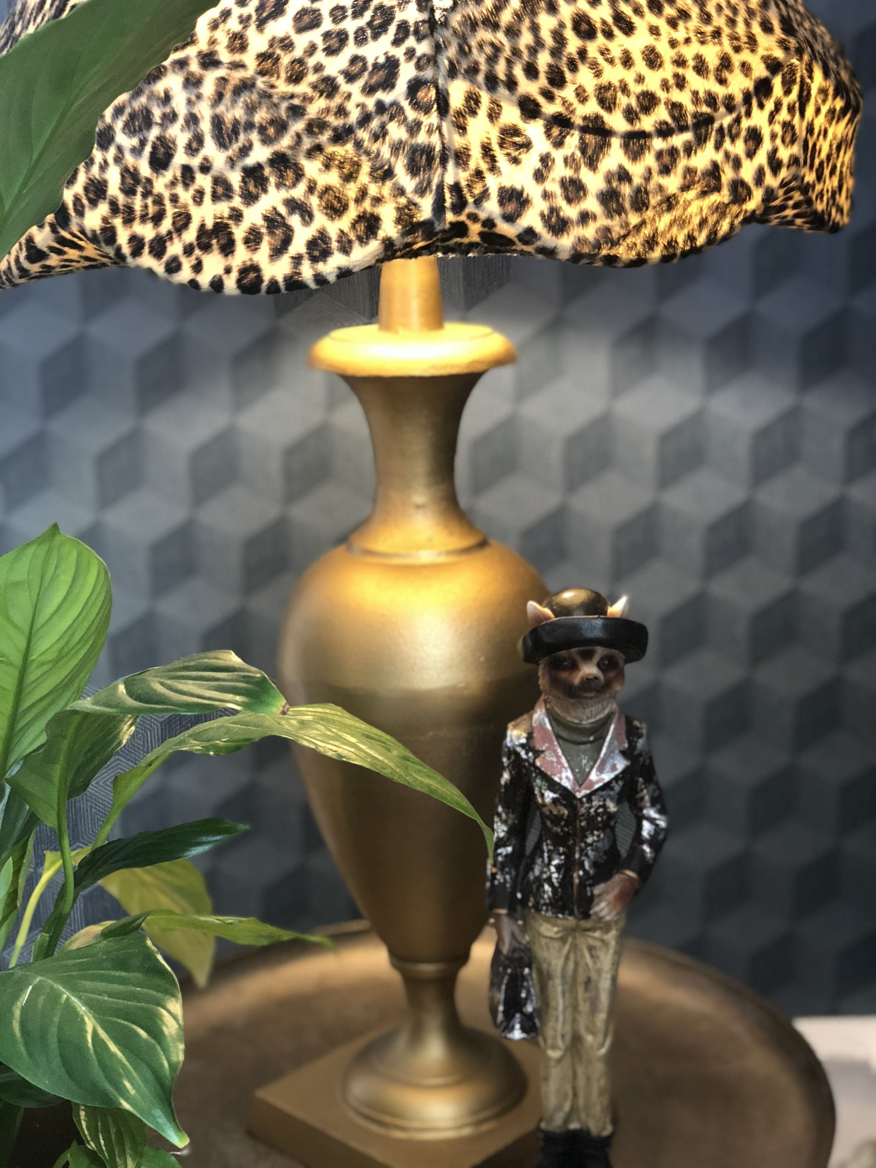 Una lámpara con pantalla de estampado de leopardo, una figurita y una planta.