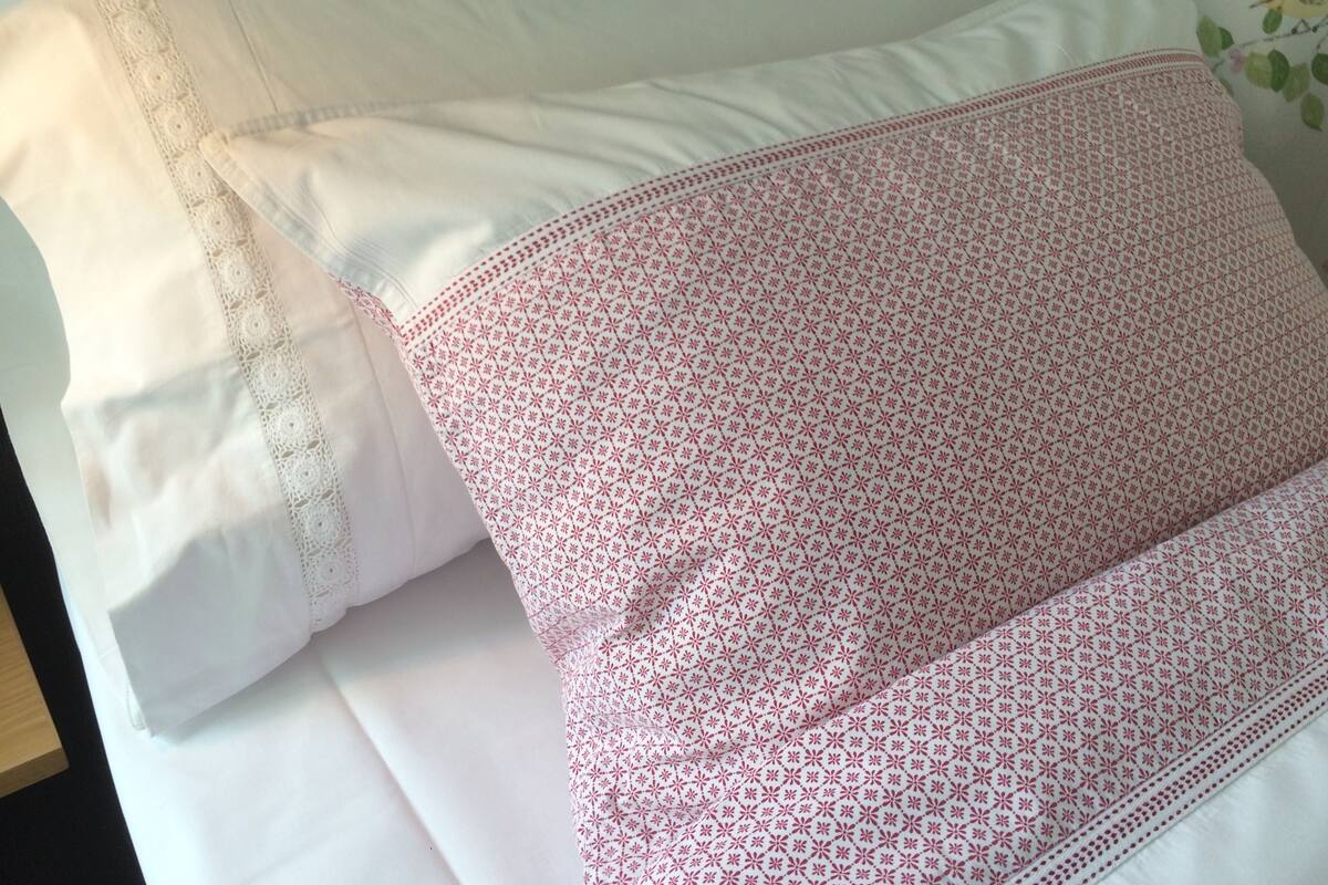 A bed with white linens and a pink patterned pillow.