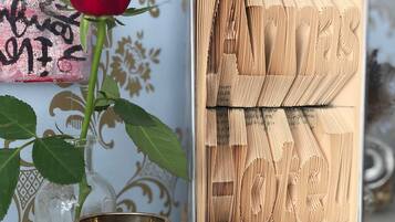 En dekorativ träpanel med ett geometriskt mönster, en glasvas med en röd ros och en guldfärgad behållare på ett bord.