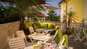 A wooden deck with white folding chairs and a table set for dining, surrounded by a wooden fence and palm trees. - Annas Hotell (Kristianstad)