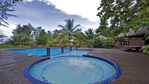 A swimming pool with a wooden deck, surrounded by palm trees and a thatched-roof structure. - Aseania Resort Pulau Besar (Pulau Besar)